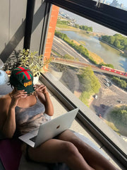 Rabiun customer on a windowsill with a laptop, wearing the Green & Leopard hat